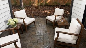 Un patio con cuatro sillas de madera y una mesa, rodeado por una valla de madera y un árbol.