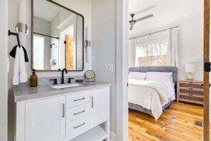 A modern bathroom with a large mirror, white cabinetry, and a shower area. - Designer Garden Home Downtown (Durham)