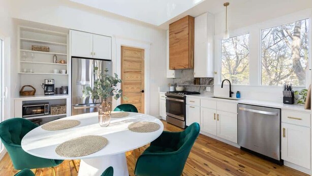Una cocina moderna con armarios blancos, una puerta de madera y un comedor con una mesa blanca y sillas verdes.