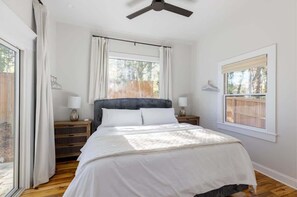 A bedroom with a bed, two bedside tables, a ceiling fan, and windows with curtains. - Designer Garden Home Downtown (Durham)