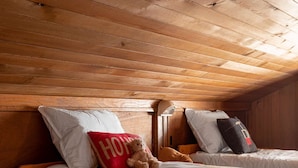 Un dormitorio acogedor con cabaña, con dos camas, vigas de madera en el techo y un osito de peluche en una de las camas.