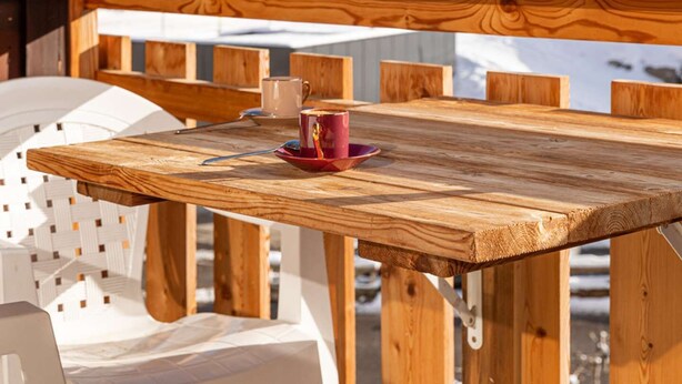 Una terraza de madera con una mesa y sillas, con vistas a un paisaje montañoso nevado.