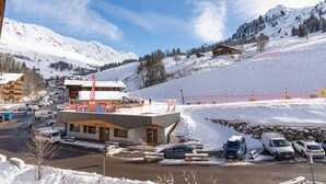 Un centro turístico en la montaña cubierto de nieve, con centro médico, zona de estacionamiento y pistas de esquí.
