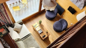 Una habitación con piso de madera, un sofá, dos sillones redondos, una mesita con una planta y una ventana que ofrece vistas a una zona de estar al aire libre.