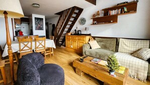 Una sala de estar acogedora con una mesa de centro de madera, un sofá y un comedor con sillas y mesa de madera. Se ve una escalera al fondo.