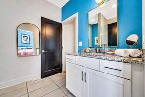 A modern bathroom with a blue accent wall, a large mirror, a dark door, and a countertop with toiletries.