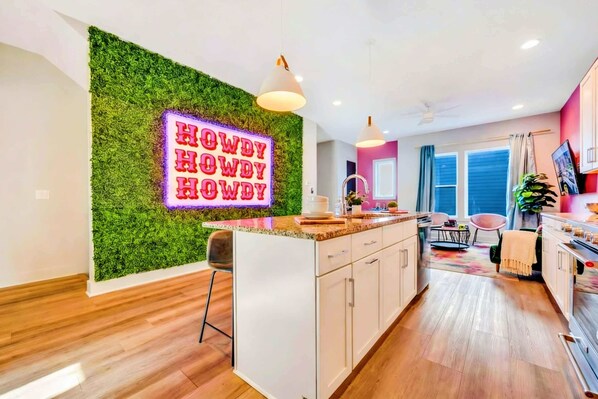 A modern kitchen with a neon sign, wooden flooring, and a green wall.