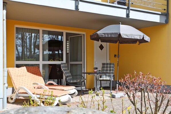 A balcony with two lounge chairs, a table, and an umbrella.