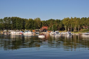 Un port de plaisance avec des bateaux amarrés, un bâtiment avec un toit rouge et, au loin, une colline boisée.