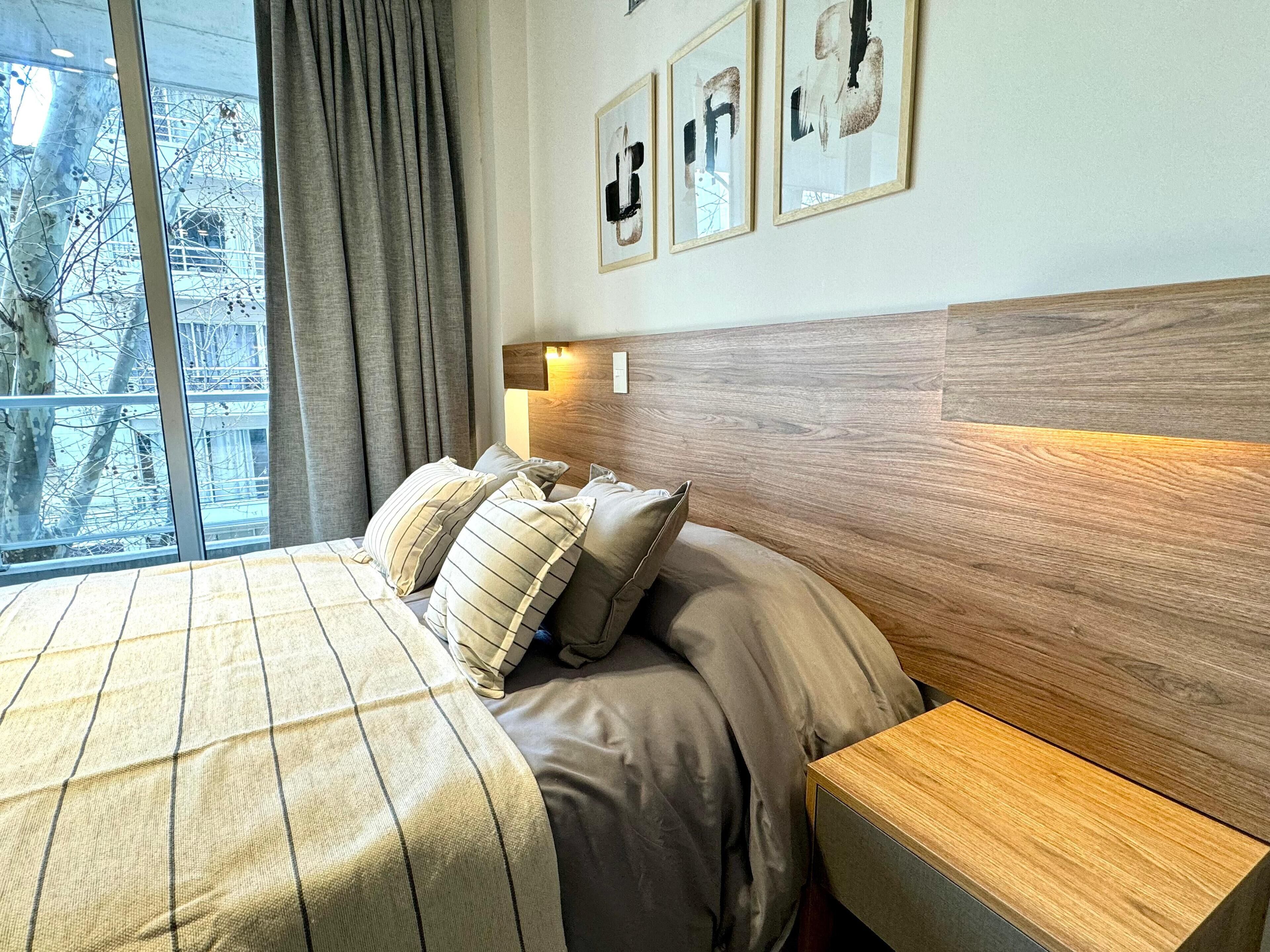 Een hotelkamer met een groot bed, een houten hoofdbord, een nachtkastje en een raam met gordijnen.