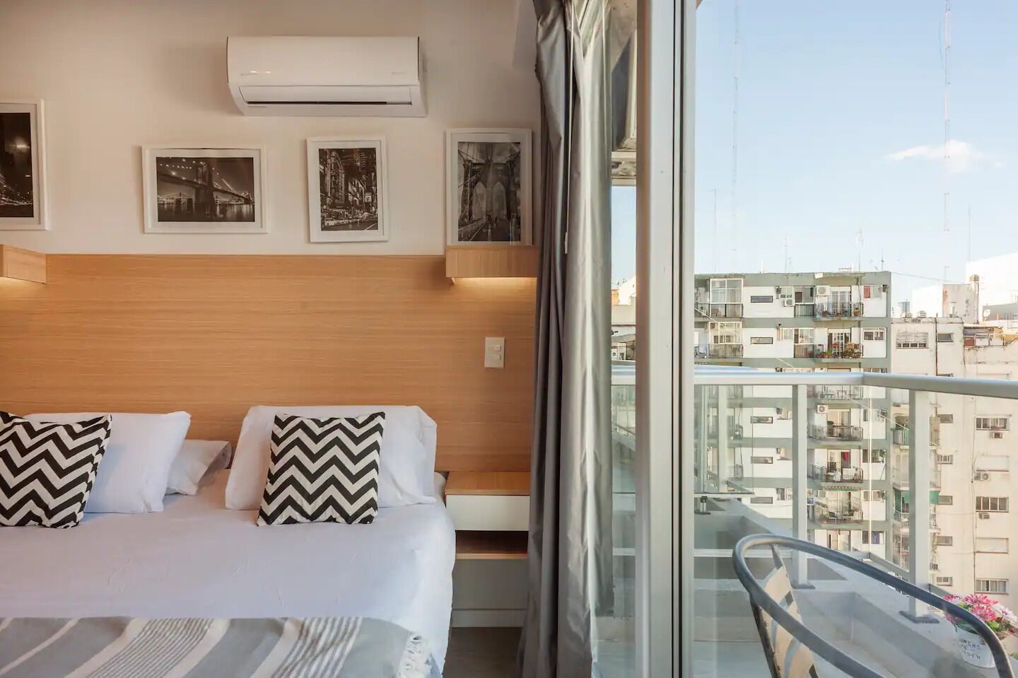 A hotel room with a bed, air conditioning unit, and framed pictures on the wall.