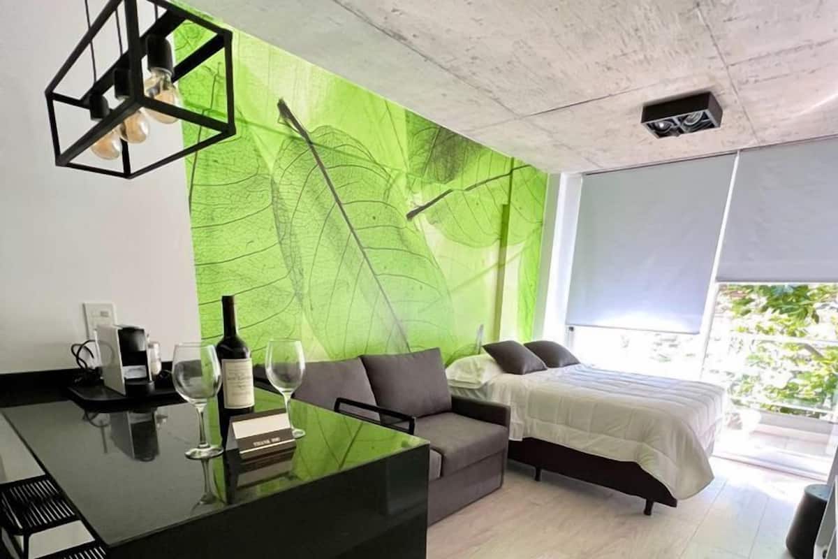 A modern, minimalist bedroom with a large bed, a small sofa, and a bar area.