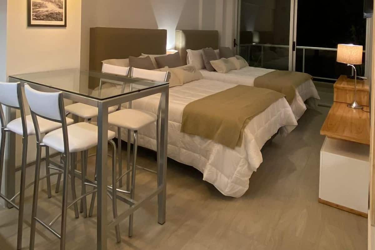 A modern bedroom with a large bed, a desk, and chairs. There are framed pictures on the wall and a window with a view.
