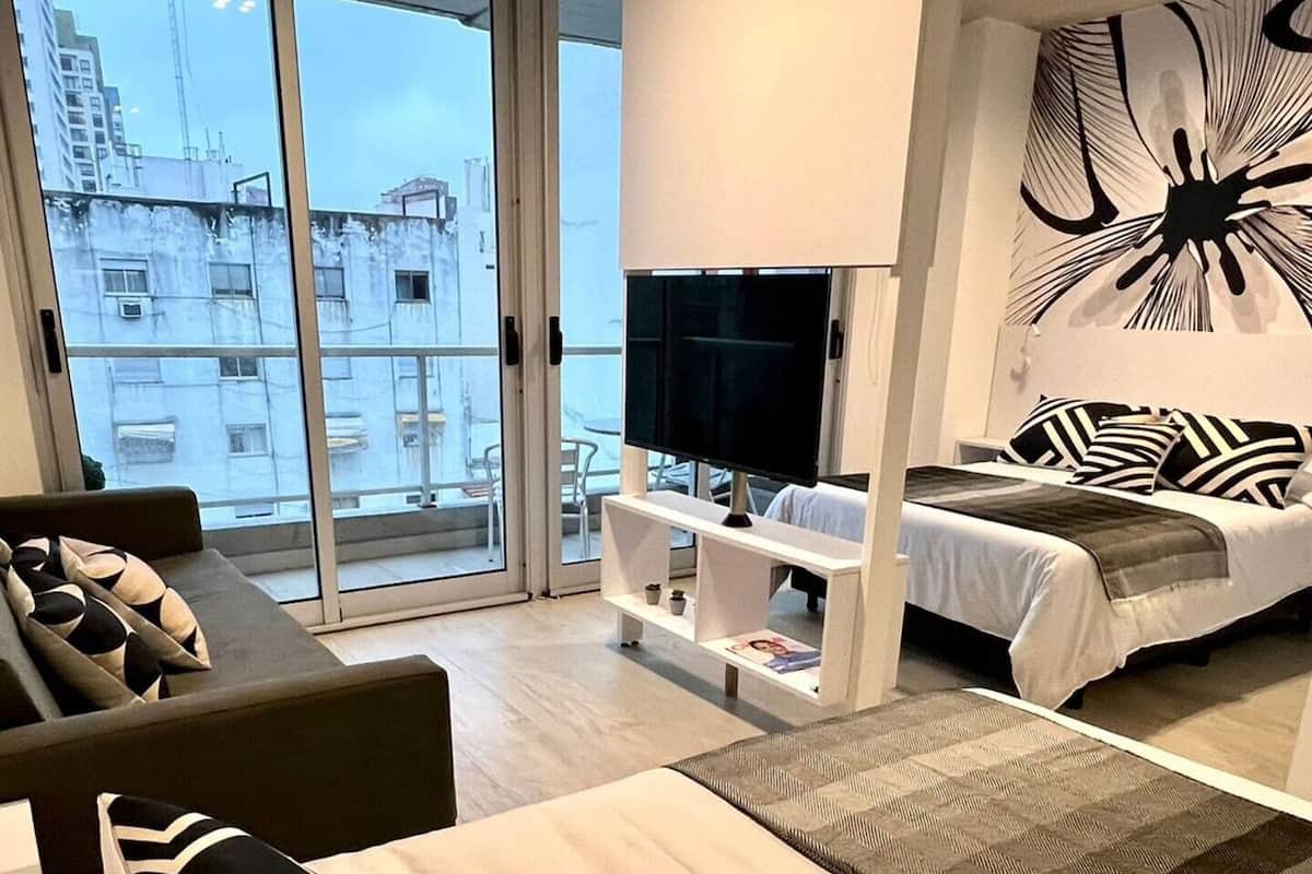 A modern hotel room with a large bed, a sofa, a TV, and a balcony with a city view.