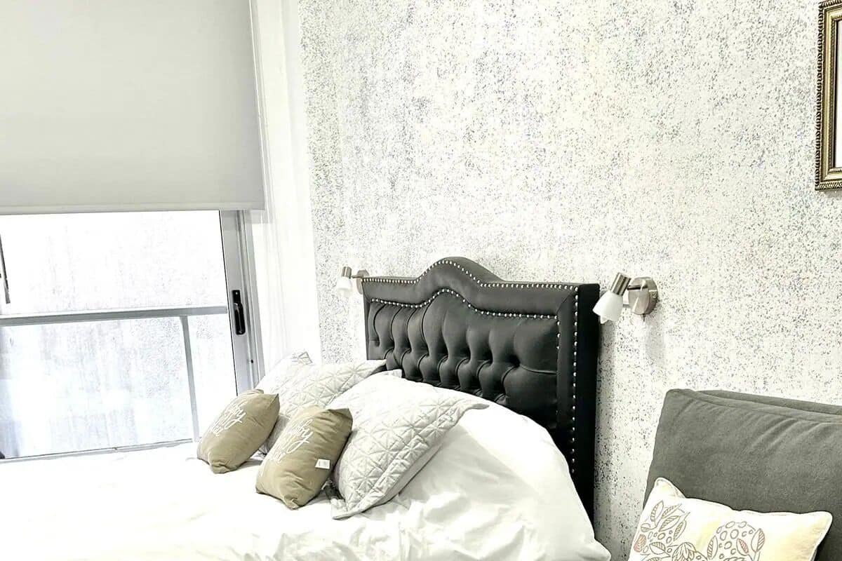 A bedroom with a bed, a grey sofa, and a patterned pillow.