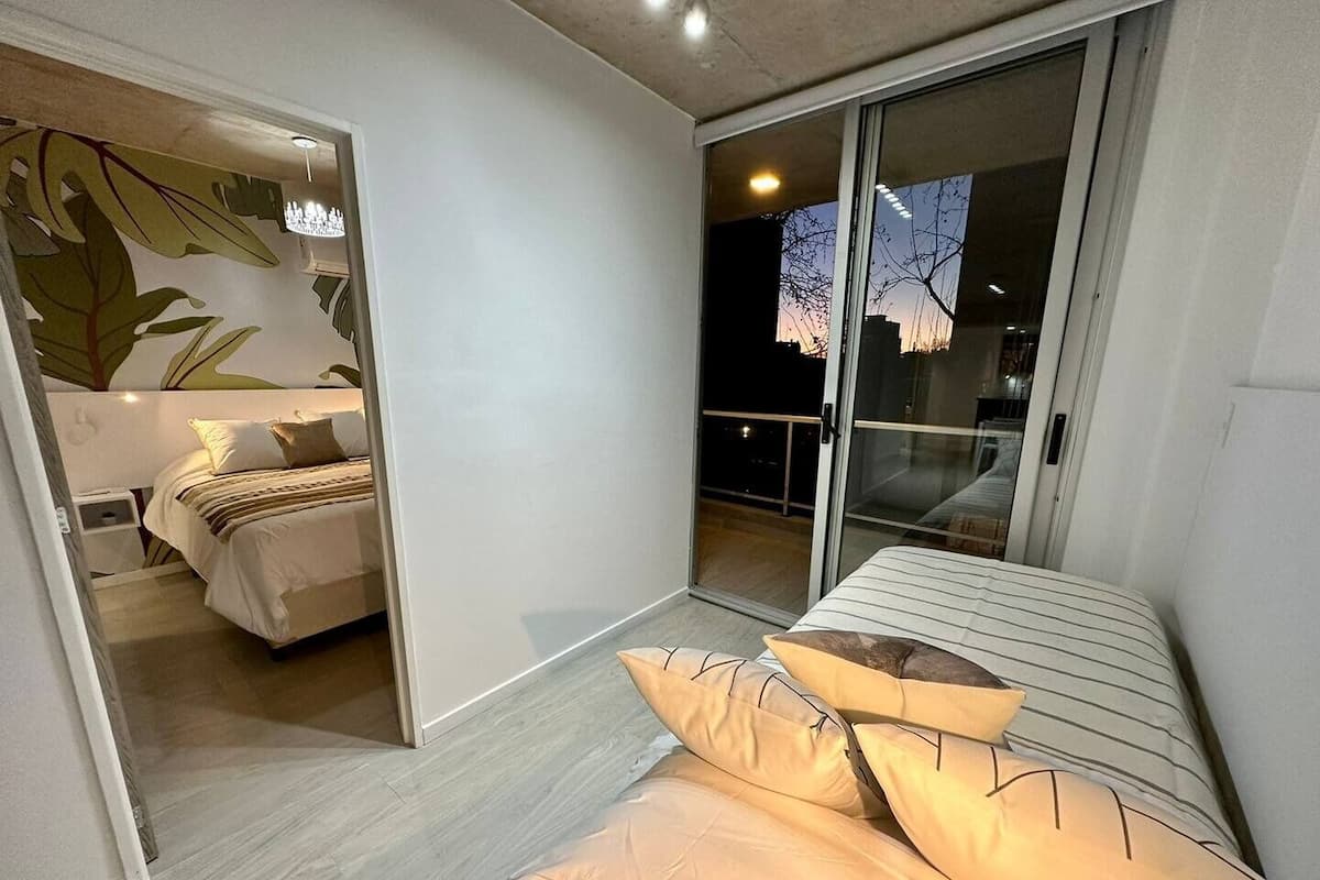 A modern bedroom with a large sliding glass door leading to a balcony, a bed with striped bedding, and a wall with a leaf pattern.