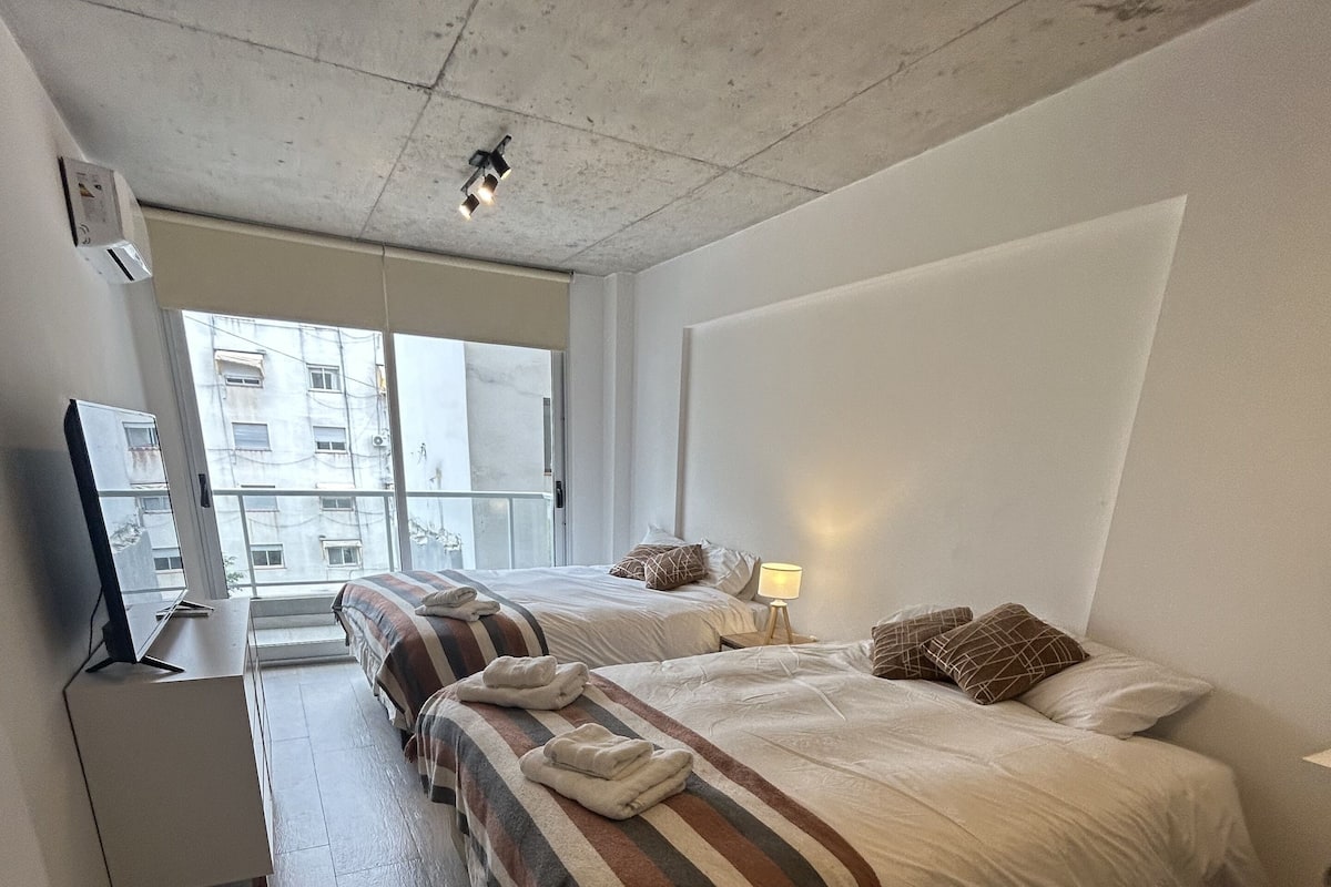 A modern hotel room with two beds, a desk, and a large window.