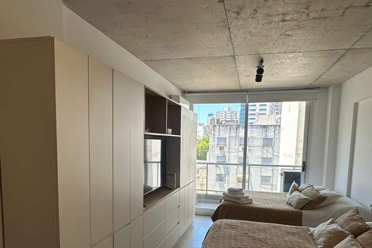 A modern bedroom with a large bed, built-in wardrobe, and a view of the city through a large window.