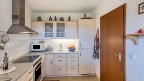 Una cocina compacta con microondas, horno y campana extractora de acero inoxidable. Hay armarios con puertas de vidrio y una puerta de madera.