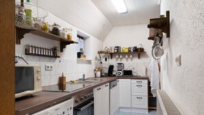 A compact kitchen with white cabinets, a microwave, a stove, and a dishwasher. There are shelves with jars and kitchen utensils. - Holiday Apartment 'Mole Valley Ranch 2' with Balcony and Wi-Fi (Elmlohe)
