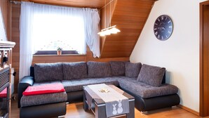 A modern living room with a sectional sofa, a small table, and a wall clock. - Holiday Apartment 'Mole Valley Ranch 2' with Balcony and Wi-Fi (Elmlohe)