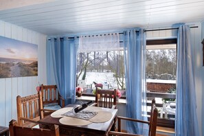 Et spiseområde med et træbord, stole og udsigt til det fri gennem et vindue med blå gardiner.