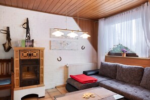 En hyggelig stue med pejs, sofa, sofabord og et vindue med gardiner.