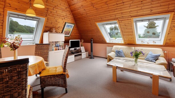 Ein gemütliches Zimmer mit Holzbalkendecke, einer Couch, einem Fernseher und einem Esstisch.