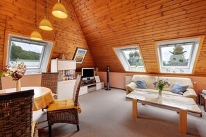 A cozy room with wooden ceiling, a sofa, a TV, and a dining table. - Apartment 'Haus Fahrenkrog' with Private Garden and Wi-Fi (Wittmoldt)