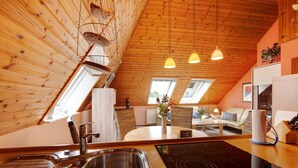 Eine Küche mit Spüle, Herd und Holzboden. Zwei Fenster und ein Essbereich mit Tisch und Stühlen sind vorhanden.