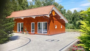 A wooden house with a red roof, large windows, and a paved driveway. - Holiday Apartment 'Ferienhaus Im Grünen' with Private Terrace, Wi-Fi and Air Conditioning (Varel)