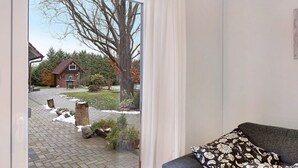 A room with a large window, a grey sofa, and a patterned pillow. - Holiday Apartment 'Ferienhaus Im Grünen' with Private Terrace, Wi-Fi and Air Conditioning (Varel)