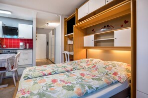 Quarto compacto com cama, cozinha compacta e pequena área de refeições.