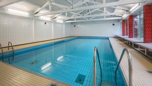 Una piscina interior con suelo de baldosas, barandillas de metal y un techo alto con vigas blancas.