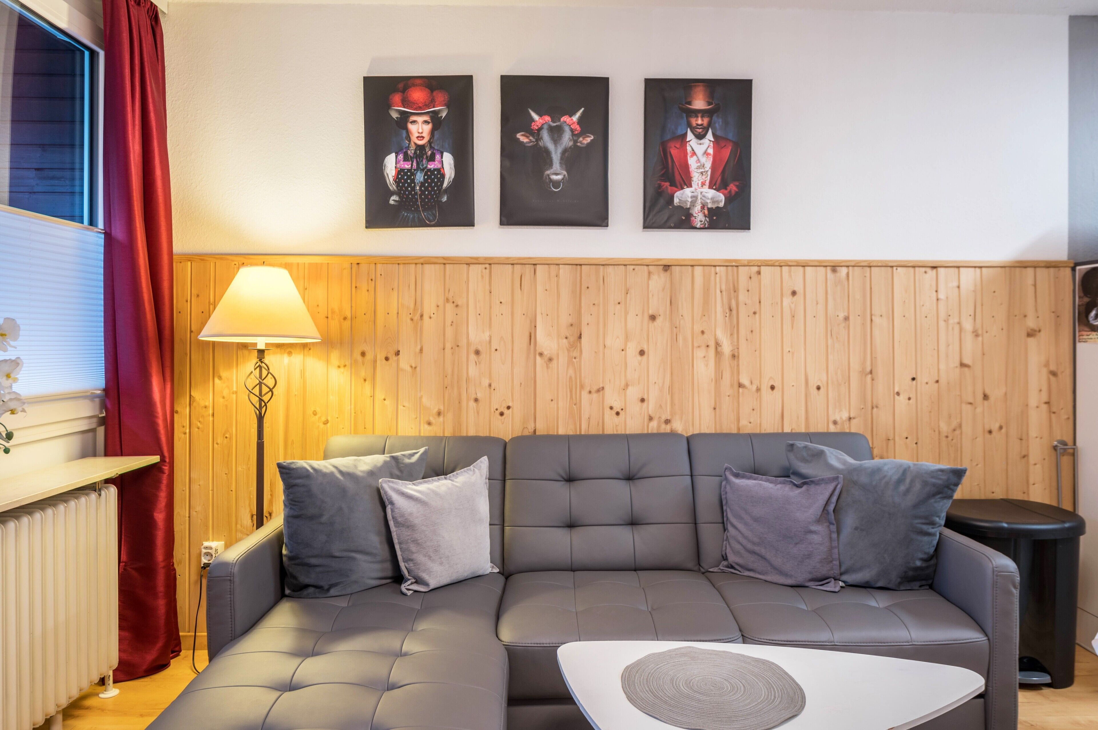 A modern living room with a sectional sofa, a lamp, and three framed artworks on the wall.