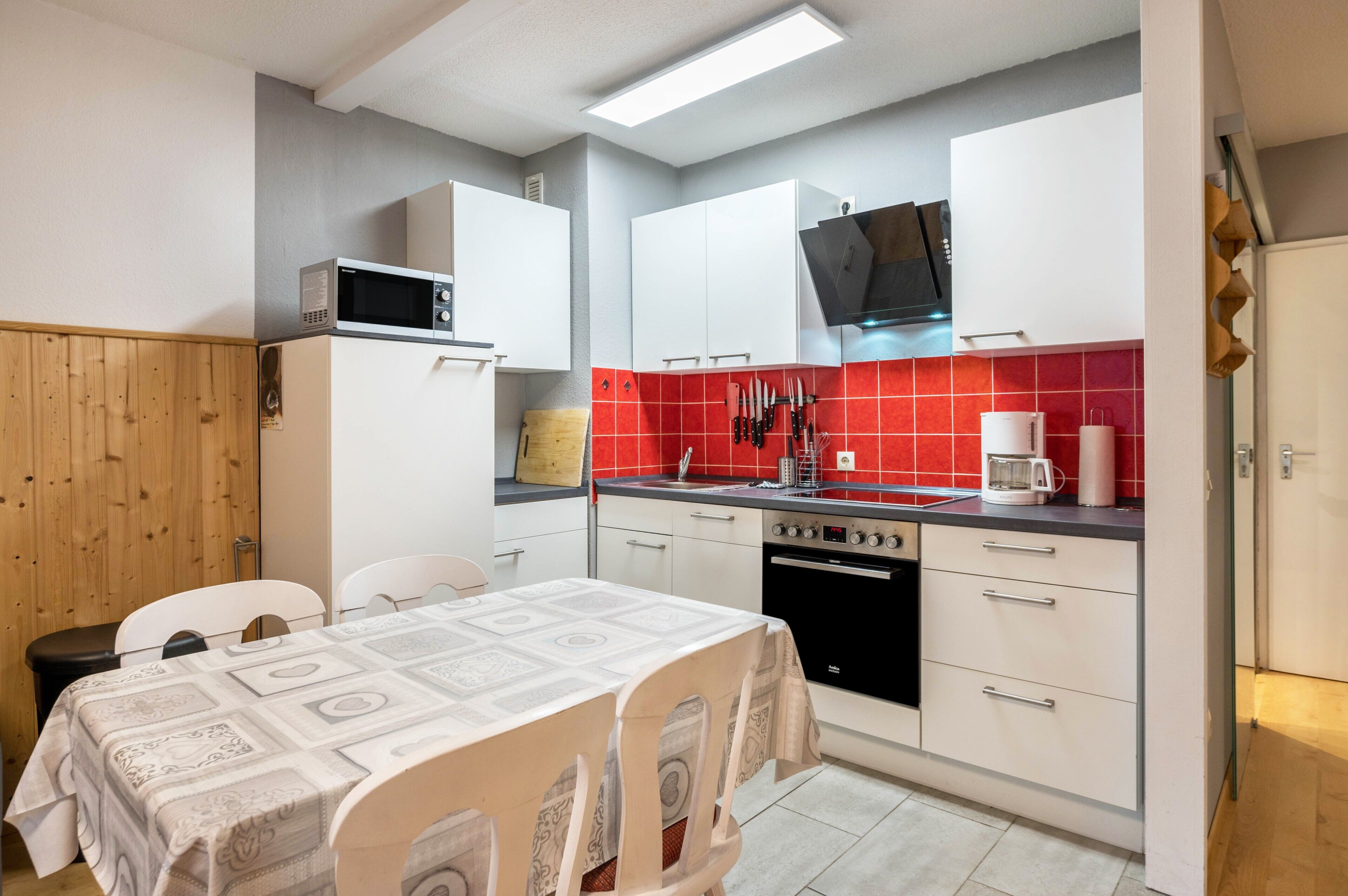 A compact kitchen with white cabinets, a microwave, a stove, and a red-tiled backsplash.