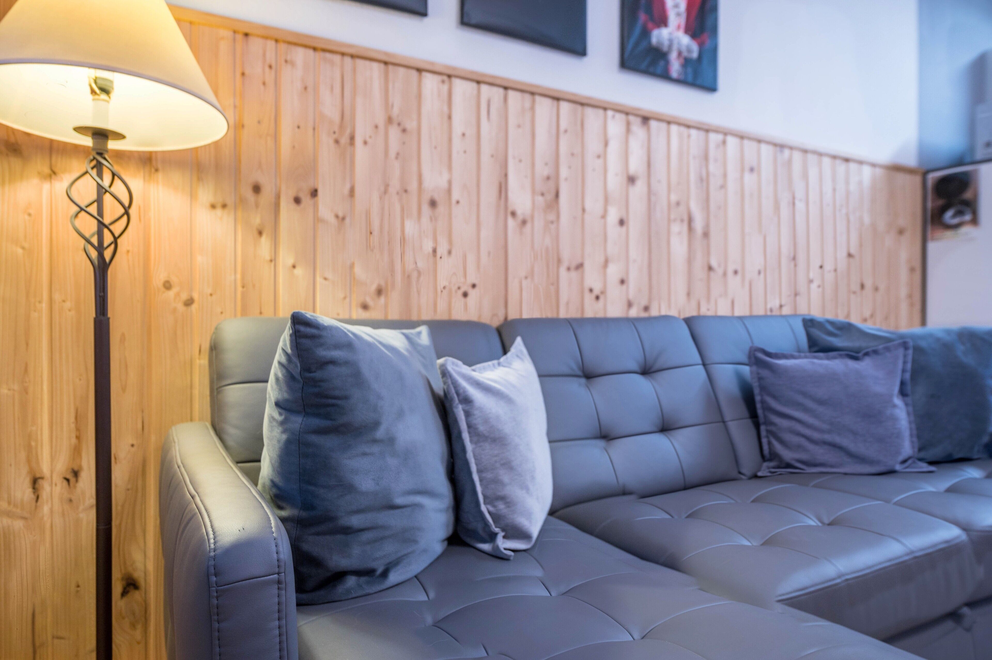 Un canapé gris avec des coussins, une lampe sur pied et un lambris en bois sur le mur.