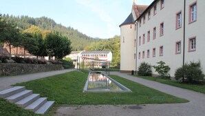 Ein Gebäude mit einem spiegelnden Wasserelement, Steinstufen und einem Weg, der zu einem weißen Gebäude mit roten Fensterrahmen führt.