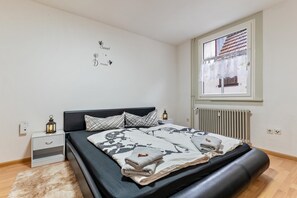 Une chambre à coucher comprenant un lit, une table de chevet, des éléments de décoration murale, une fenêtre et un radiateur.