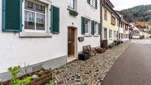Eine Reihe traditioneller europäischer Gebäude mit weißen Wänden und grünen Fensterläden, eine Kopfsteinpflasterstraße und eine Bank davor.