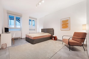 Un dormitorio moderno con cama, escritorio, silla y ventana.