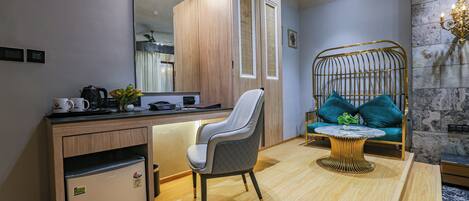 A compact hotel room with a kitchenette, a seating area with a sofa and a small table, and a large mirror above the counter.
