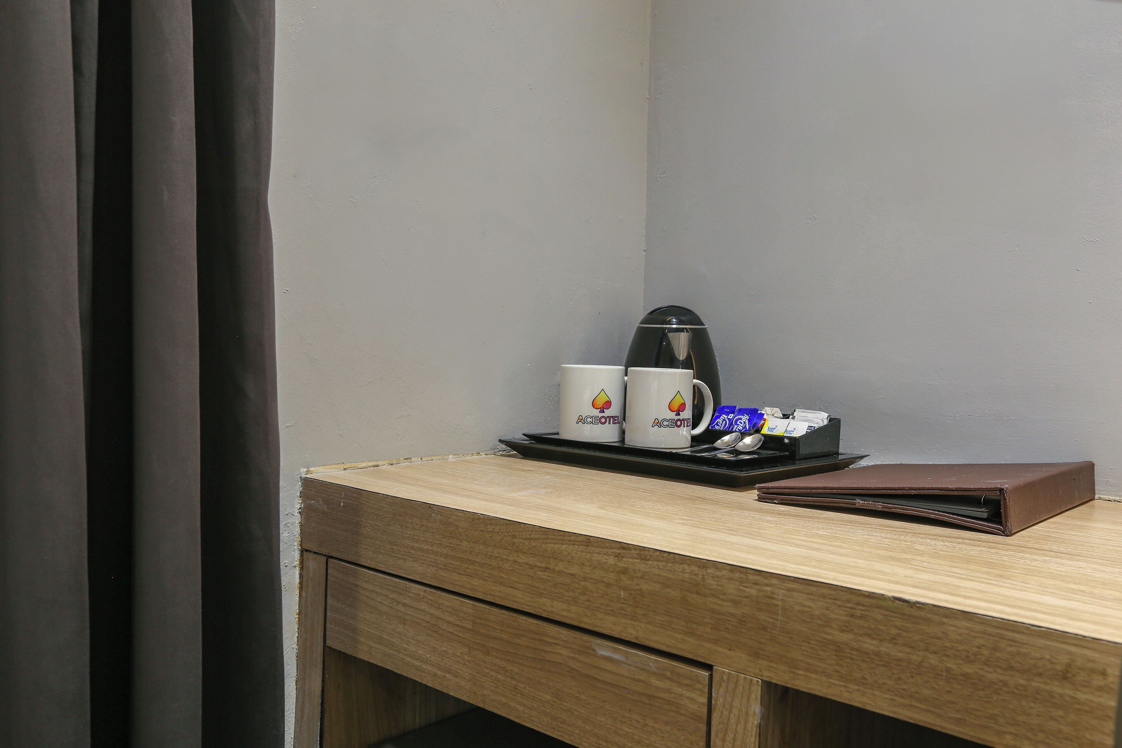 A wooden desk with a coffee maker, two mugs, a tray, and a brown folder.