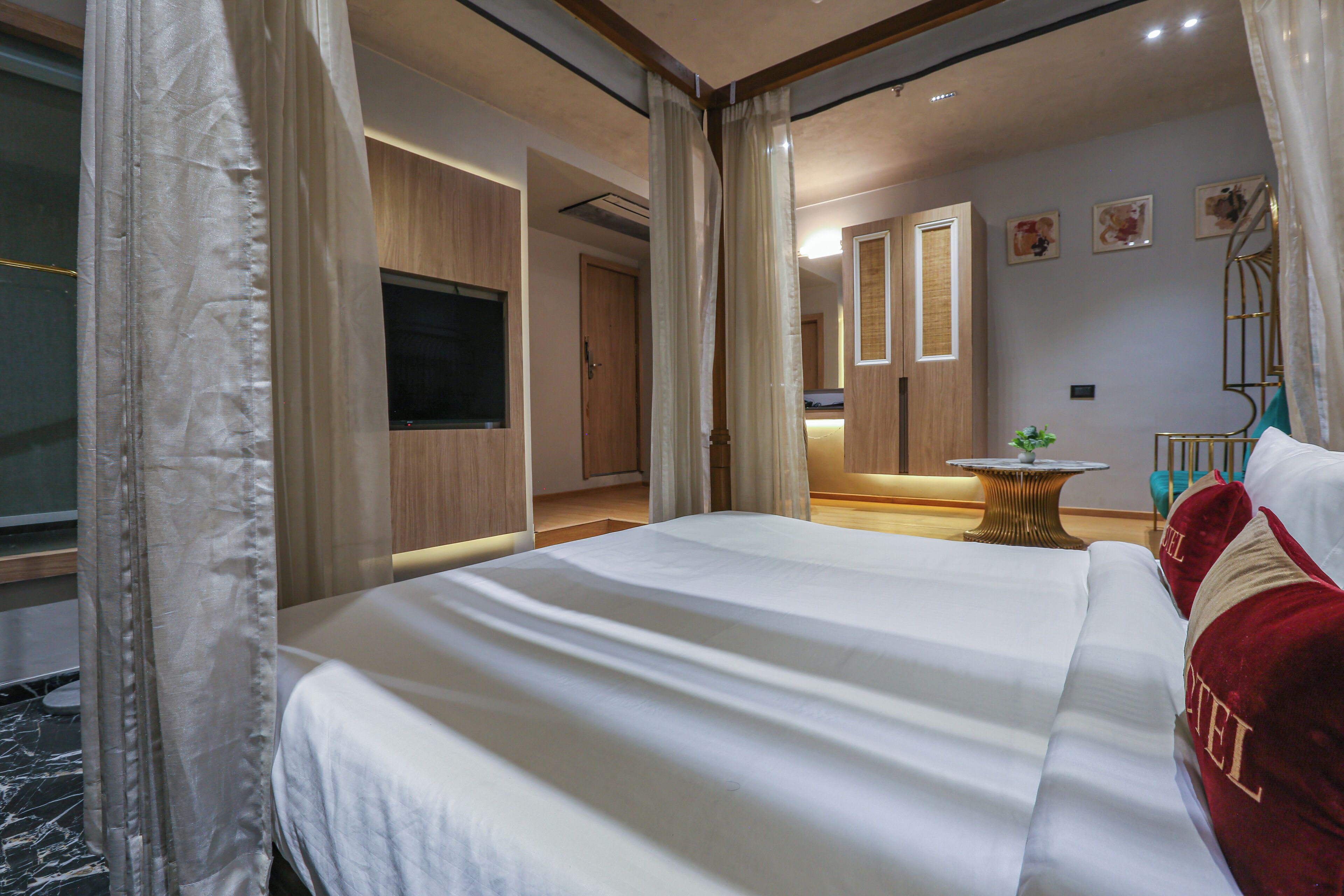 Habitación de hotel con una cama grande, televisión, escritorio con silla y una mesita con planta.