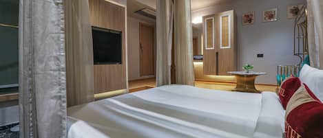 Habitación de hotel con una cama grande, televisión, escritorio con silla y una mesita con planta.