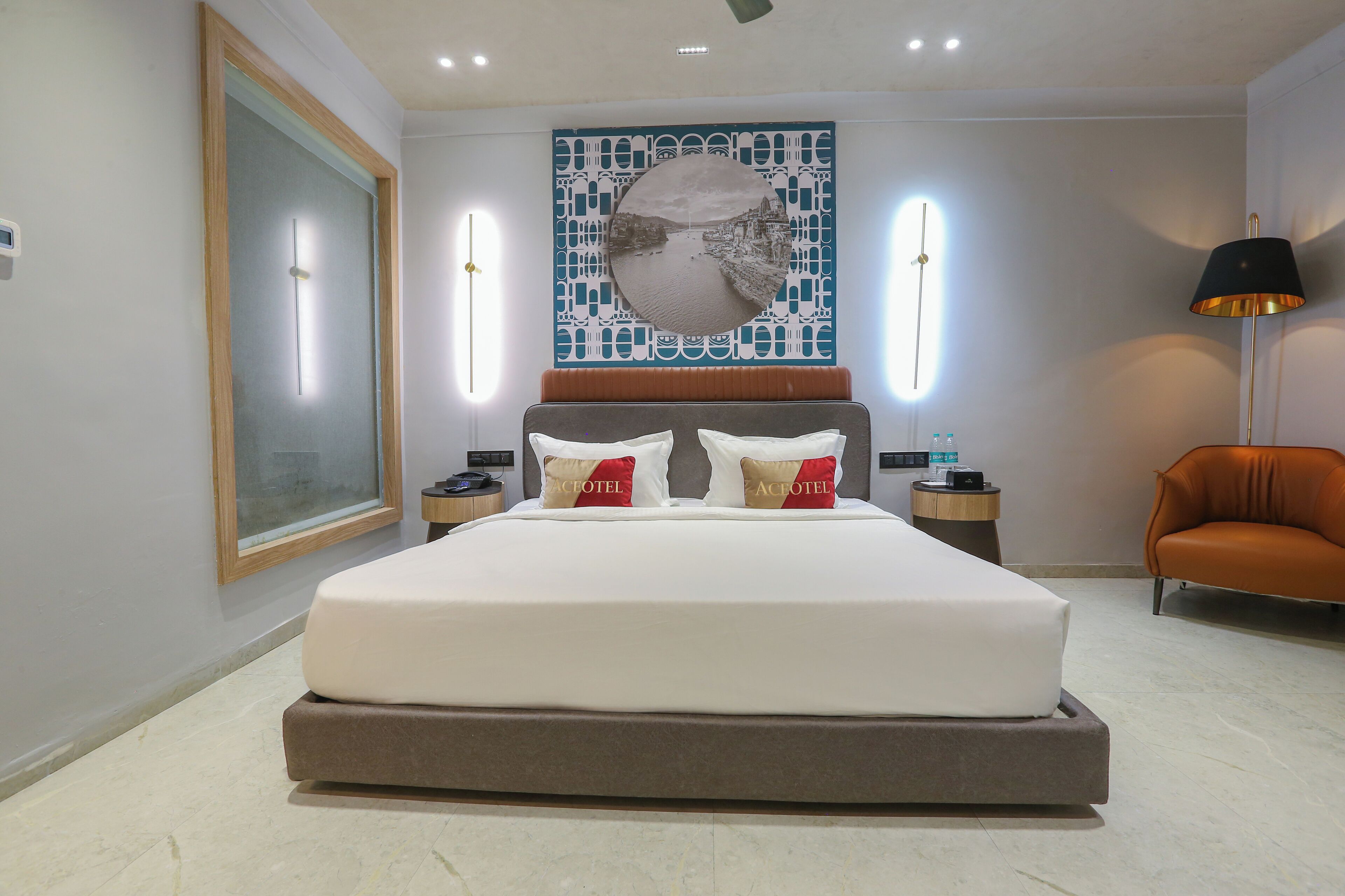 Una habitación de hotel moderna con una cama grande, una mesita de noche, una lámpara de pared y un cuadro enmarcado.