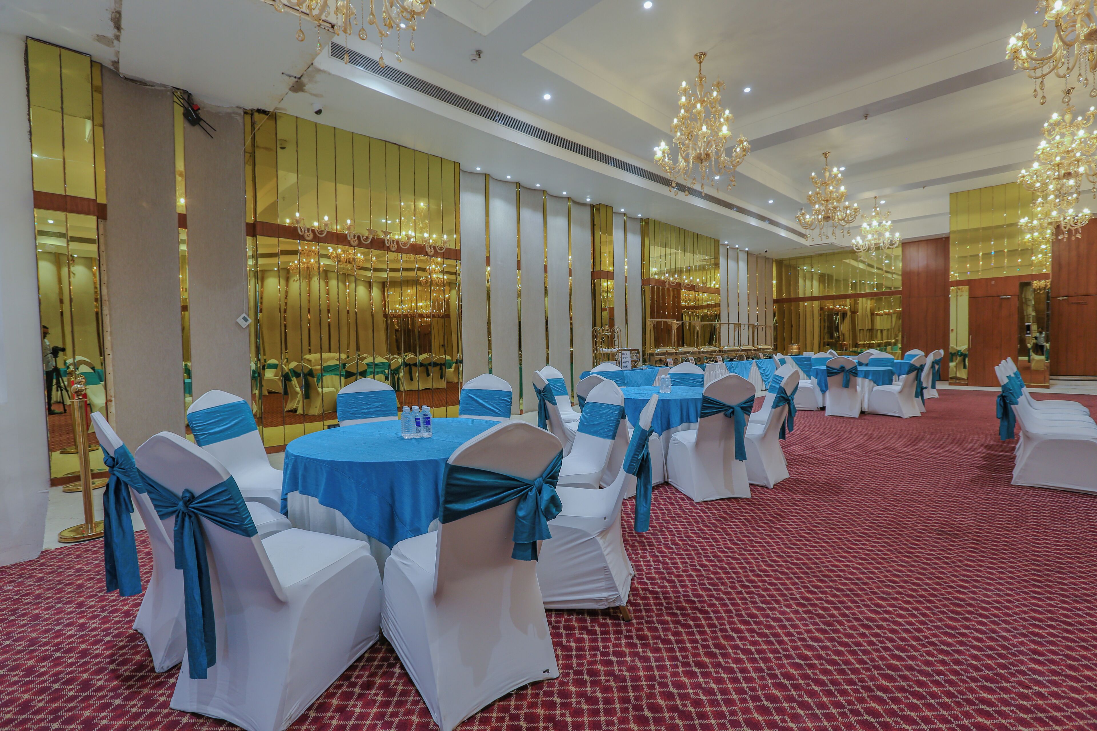 A banquet hall with round tables and white chairs, blue sashes, and chandeliers.