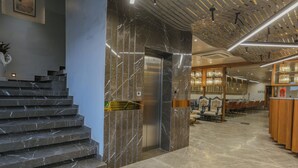 A modern lobby with marble stairs, an elevator, and a dining area with wooden furniture. - Aceotel Select Aria - A Luxury Boutique Hotel (Bhopal)