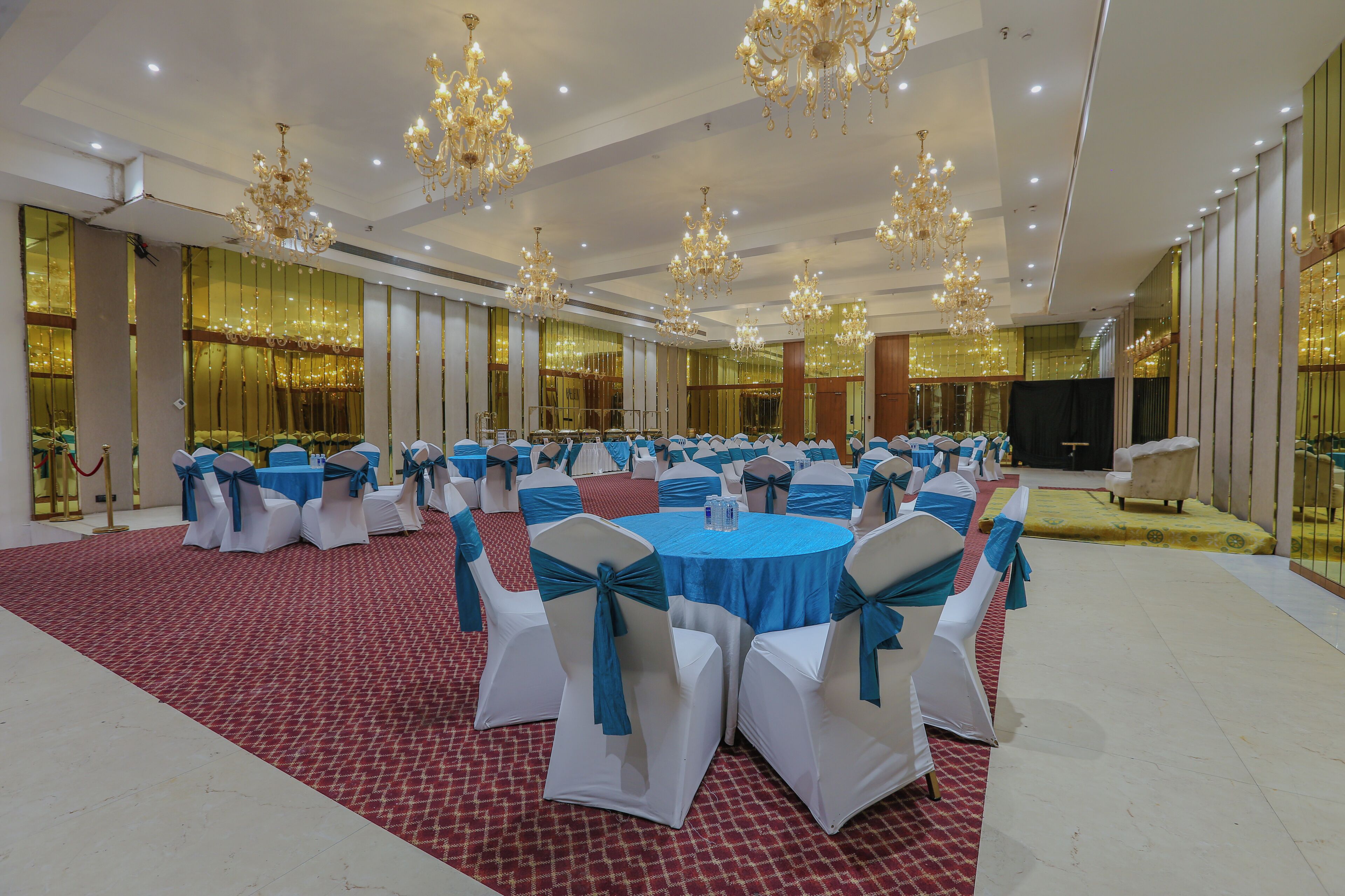 A banquet hall with round tables and chairs, chandeliers, and a red carpet.