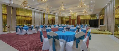 A banquet hall with round tables and chairs, chandeliers, and a red carpet.